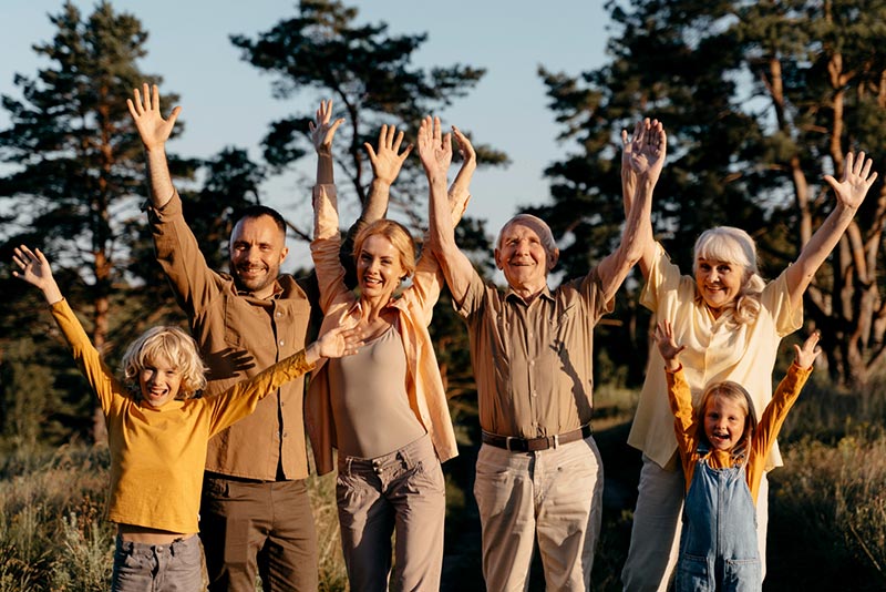Dans le jardin familial, plusieurs générations se réunissent dans une ambiance de bonheur et d'épanouissement, levant tous les bras au ciel dans un geste de célébration. Cette image évoque la puissance des liens familiaux, où chacun trouve sa place dans une atmosphère de complicité et de joie partagée.