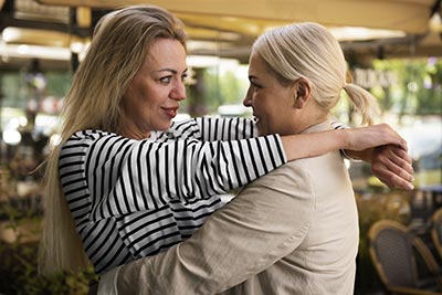 Deux femmes s'enlacent, illustrant l'importance des gestes simples de gentillesse au quotidien pour renforcer non seulement sa positivité, mais aussi celle des autres.