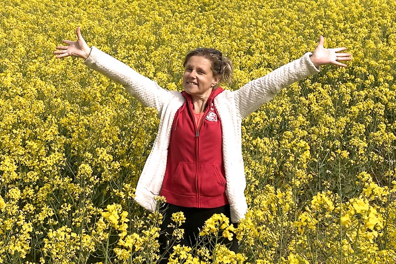 Béa, la fondatrice de Femmes en Harmonie, rayonne de bonheur dans les dunes avec la mer en arrière-plan. Avec un grand sourire, elle lève les bras vers le ciel, symbolisant l'importance de cultiver une attitude positive et d'embrasser la vie avec gratitude.