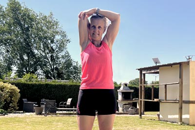 Par un beau soleil et un magnifique ciel bleu, Béa, la fondatrice de Femme en harmonie, est dans son jardin en tenue de sport à faire des exercices d'étirements.
