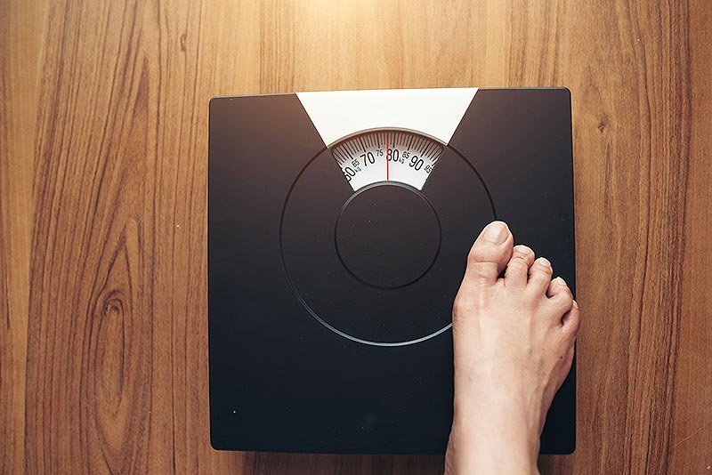 Photo d'un pèse-personnes avec le pied d'une femme prête à monter dessus, illustrant l'importance des aliments riches en protéines pour optimiser la satiété et la gestion du poids.