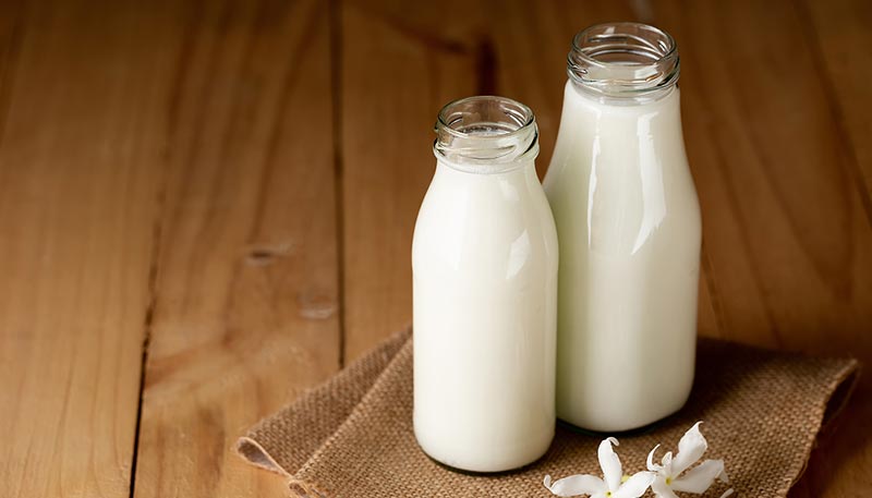 Deux bouteilles de lait en verre posées sur un parquet, illustrant une source riche en protéines pour une alimentation équilibrée.