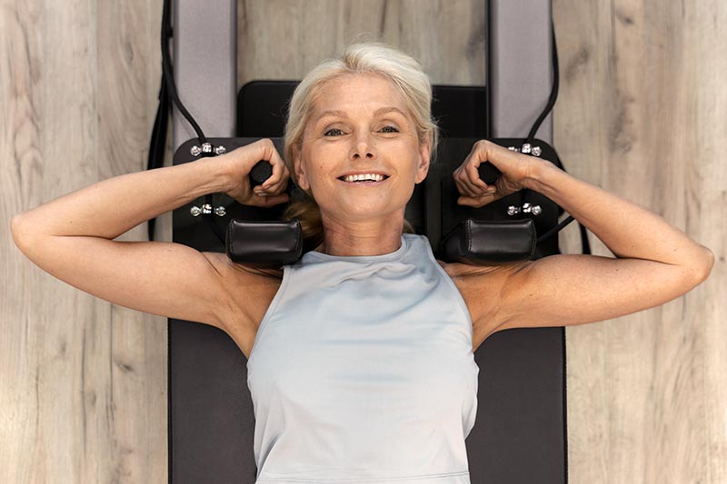 Une femme blonde aux cheveux courts, portant un tee-shirt bleu ciel, fait de la musculation, illustrant la complémentarité du renforcement musculaire avec une alimentation riche en protéines.