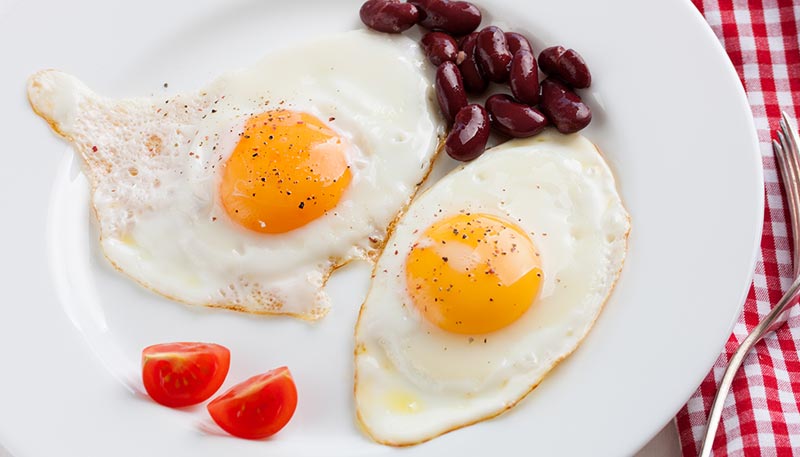 Deux œufs sur le plat dans une assiette blanche posée sur une nappe à carreaux rouge et blanc, illustrant une source riche en protéines animales pour un repas équilibré.