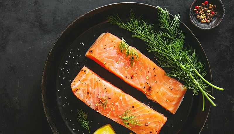 Deux pavés de saumon grillé sur une poêle avec des herbes aromatiques, illustrant une source riche en protéines animales et oméga-3.