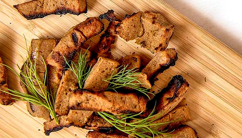 Morceaux de seitan grillé avec des herbes aromatiques sur une planche en bois