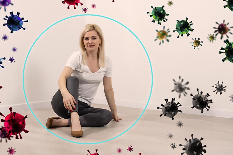 Une femme d'une quarantaine d'années, blonde aux cheveux longs, en pantalon beige et tee-shirt blanc, est assise entourée d'un cercle avec des virus virevoltant à l'extérieur, illustrant l'importance des aliments riches en protéines pour un système immunitaire fort.