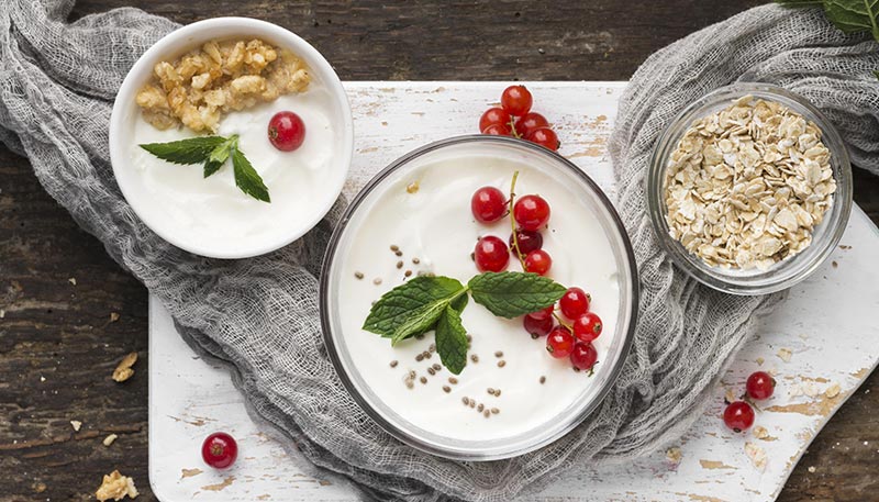 Deux bols de yaourt grec, l'un plus grand que l'autre, garnis de morceaux de fruits et de baies, illustrant une collation riche en protéines.