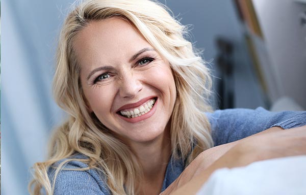 Gros plan sur une femme blonde d'environ quarante-cinq ans avec un grand sourire, portant un pull bleu. Cette photo illustre comment les affirmations positives peuvent améliorer le bien-être général.
