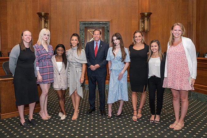 Simone Biles, entourée d'autres victimes de Larry Nassar, lors de leur visite au Sénat des États-Unis en 2021. Cette photo capture un moment crucial où Simone et les autres survivantes plaident pour des réformes afin de prévenir les abus dans le sport. Leur rencontre avec les législateurs met en lumière l'impact profond des abus subis et souligne le courage de Biles dans sa lutte pour la justice et la protection des jeunes athlètes.
