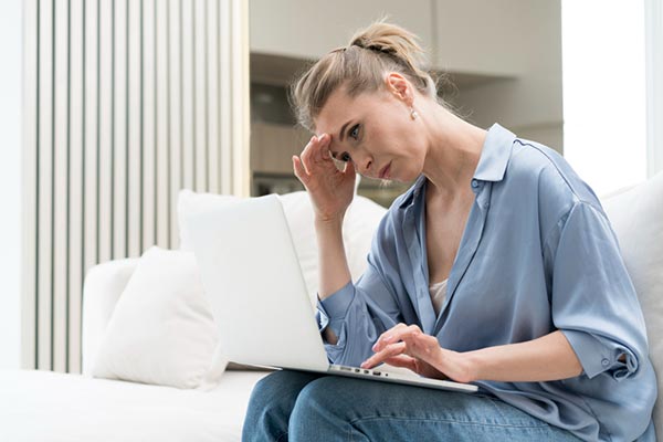 Femme d'une quarantaine d'années, blonde, assise dans un canapé, se tenant la tête avec une expression de fatigue. Illustration des signes subtils de l'inflammation chronique, comme la fatigue persistante, pouvant être atténuée par des aliments anti-inflammatoires et un mode de vie équilibré.
