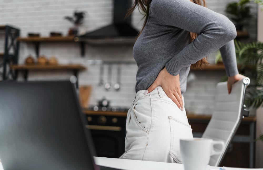 Femme de cinquante ans se levant d’une chaise et se tenant le dos en raison de douleurs, illustrant l'impact de l'inflammation chronique sur le corps.