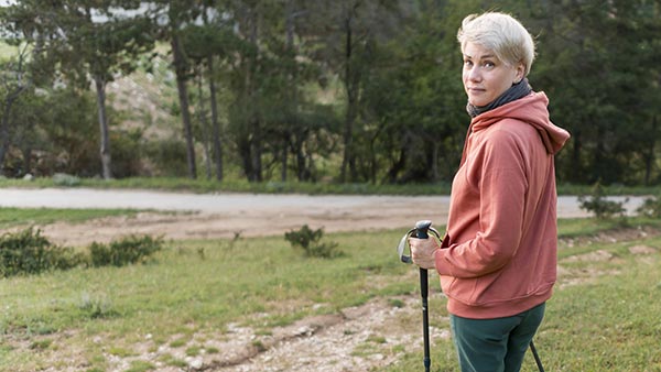 Jeune femme de 45/50 ans, cheveux courts, pratiquant la marche avec des bâtons dans la campagne, une activité bénéfique pour réduire les symptômes de la ménopause.