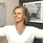 Béa, fondatrice de Femmes en Harmonie, souriante et pleine d'énergie, montre ses biceps pour illustrer les bienfaits des aliments énergétiques qui favorisent la forme et la vitalité.