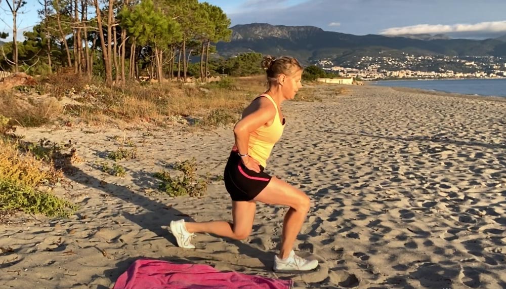 Béa, fondatrice de Femmes en Harmonie, effectue des fentes avant sur une plage au lever du soleil pour montrer comment brûler des calories et renforcer les muscles après 50 ans.