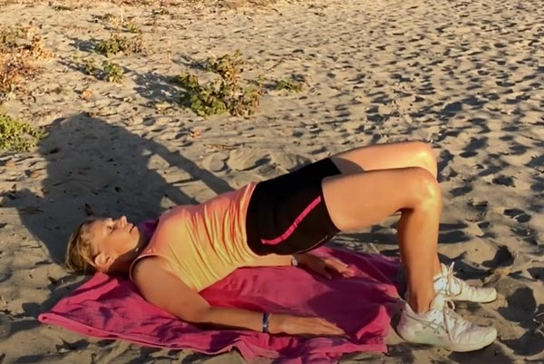 Béa, fondatrice de Femmes en Harmonie, effectue un pont fessier sur la plage pour illustrer comment brûler des calories et renforcer les fessiers, les ischio-jambiers et le bas du dos. Cet exercice simple aide à améliorer la stabilité du bassin et à soulager les douleurs lombaires après 50 ans.