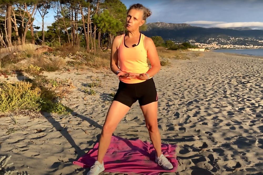 Béa, la fondatrice de Femmes en Harmonie, sur une plage, montre l’exécution d’un exercice pour brûler des calories et renforcer les muscles des cuisses et des fessiers.