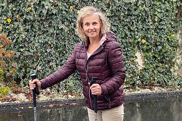 Béa, fondatrice de Femmes en Harmonie, marche en ville avec des bâtons de marche sous la pluie, souriante. Cette image illustre les bienfaits de la marche pour rester active, améliorer la forme physique et profiter du plein air, même par mauvais temps.