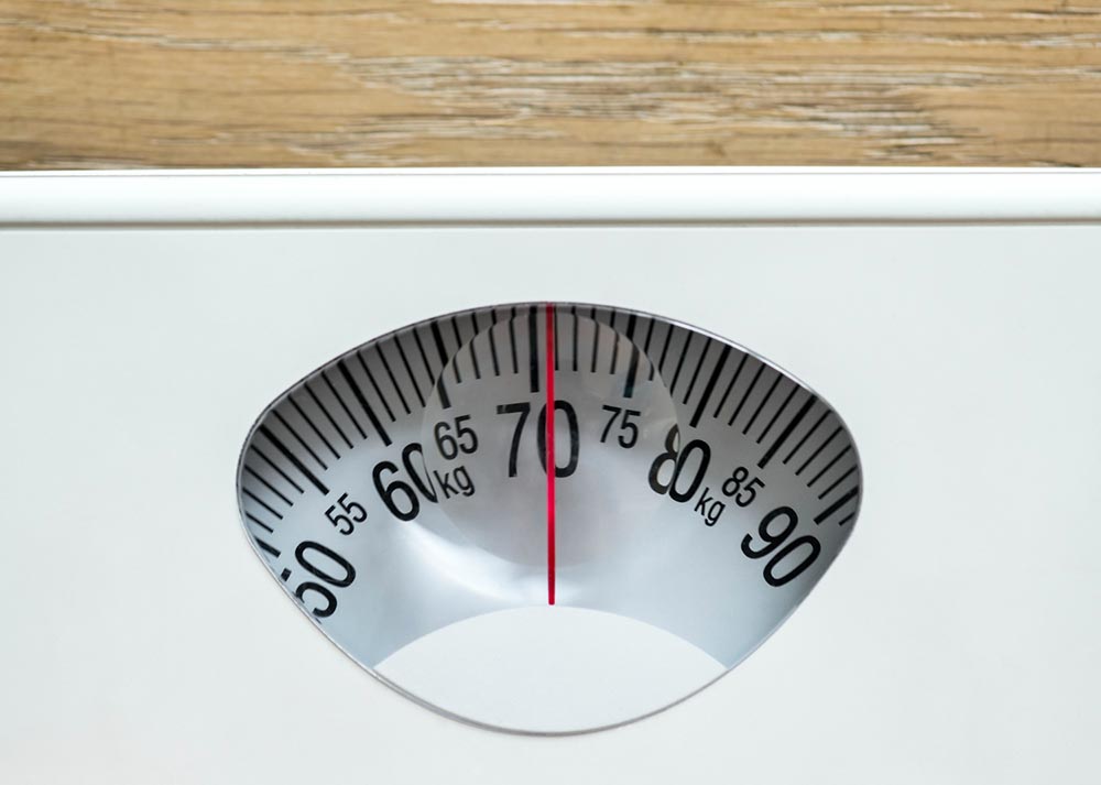 Balance affichant 70 kg, illustrant les causes cachées de la prise de poids, notamment les changements hormonaux et le ralentissement du métabolisme chez les femmes de plus de 45 ans.
