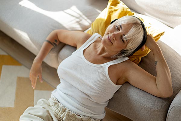 Femme d'une cinquantaine d'année se relaxant avec des écouteurs, illustrant l'importance de pratiquer des techniques simples comme écouter de la musique et se relaxer pour réduire le stress et mieux gérer son poids avec l'âge.