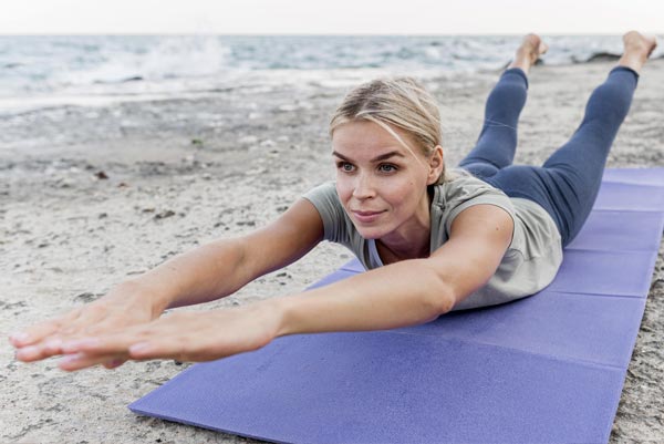 Femme pratiquant l'exercice 'Superman' sur un tapis de yoga en plein air, illustrant l'importance des exercices de renforcement musculaire pour prévenir la prise de poids et renforcer les muscles après 45 ans.