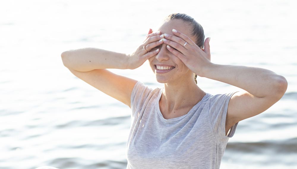 Femme d'environ 4( ou 50 ans, souriante les mains sur les yeux, illustrant l'importance de la gestion du stress pour maintenir un poids équilibré et réduire l'impact du cortisol, particulièrement après 45 ans.