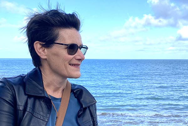 Sandra regardant l'horizon au bord de la mer, symbolisant la quête de paix et de résilience.