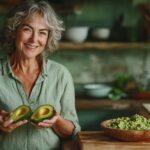 Femme de 55 ou 60 ans avec de beau cheveux longs et gris et un grand sourire dans sa cuisine, transformant des avocats trop mûrs en délices culinaires, un geste anti-gaspi et écoresponsable.