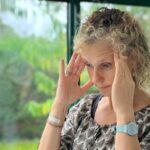 Béa, la fondatrice de Femmes en Harmonie, se tient la tête dans les mains, exprimant une réflexion intense. Cette image illustre les moments où les pensées deviennent envahissantes et montrent la nécessité de découvrir comment arrêter de trop penser. L’article propose quatre clés efficaces pour apaiser le mental et alléger l’esprit.