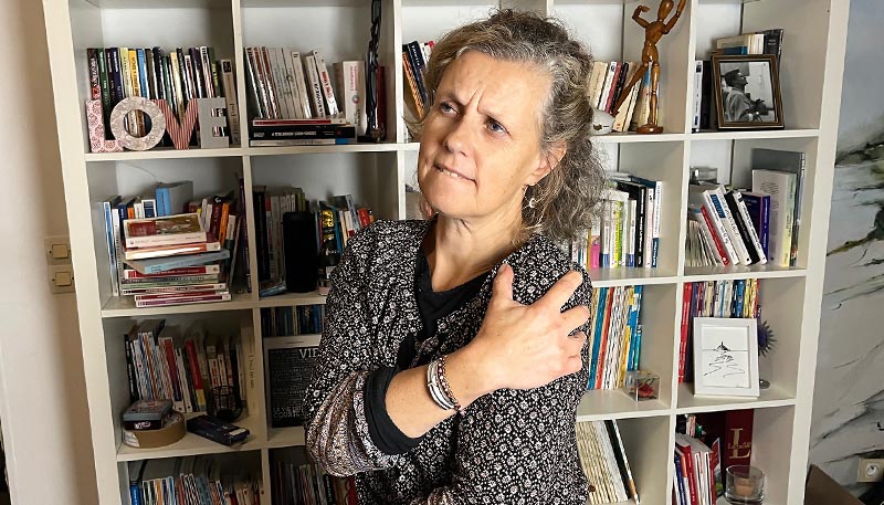 Béa, fondatrice de Femmes en Harmonie, tient son épaule avec une expression de douleur, illustrant les tensions et douleurs aux épaules et au cou fréquentes chez les femmes.