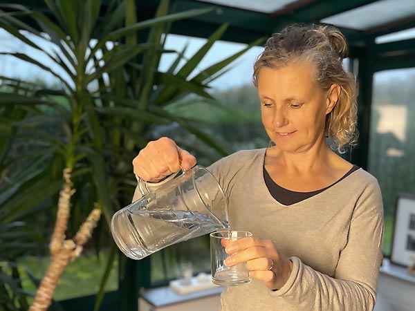 Béa, fondatrice de Femmes en Harmonie, versant un verre d’eau pour illustrer les bienfaits de l’hydratation sur la santé, notamment pour réduire la fatigue, améliorer la digestion et hydrater la peau après 45 ans.