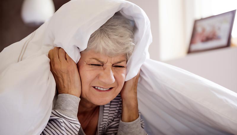 Une femme d'environ 60 ou 65 ans,  allongée sur le ventre dans son lit, les drap sur sa tête et très énervée de ne pas parvenir à dormir.