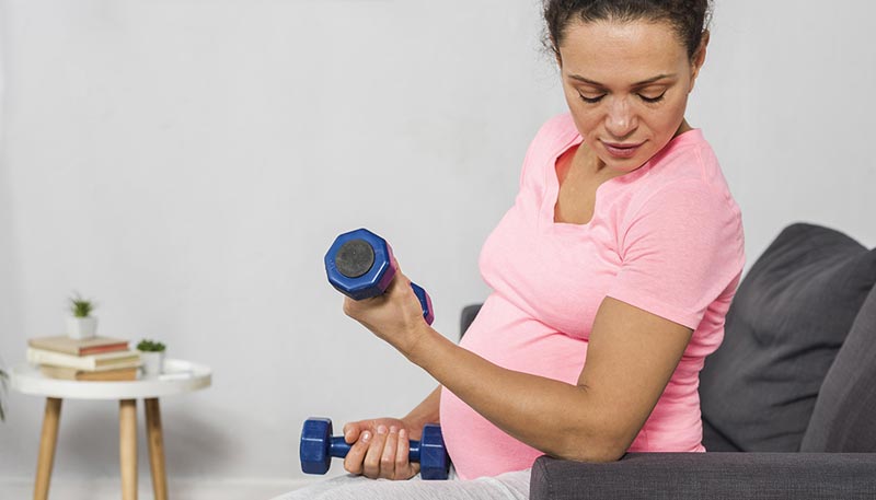 Une femme réalisant un exercice avec des haltères légers sur le canapé de son salon, 