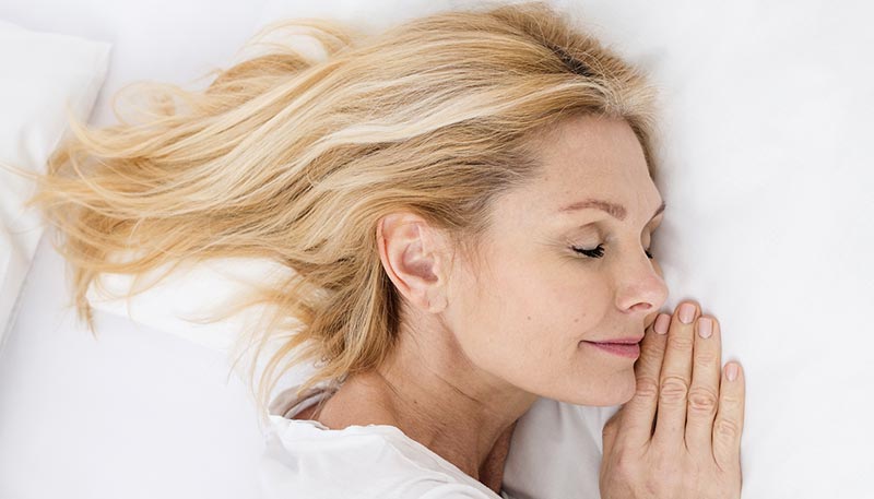 Une femme de 50 ans dormant paisiblement avec un léger sourire sur les lèvres dans un lit, 