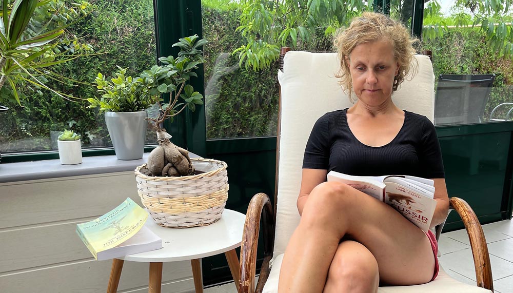 Béa en pleine lecture confortablement installée dans sa véranda et entourée de verdure. Elle illustre parfaitement comment intégrer la lecture dans son quotidien pour mieux profiter de ses bienfaits.