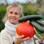 Béa, fondatrice de Femmes en Harmonie, tenant des légumes frais : potimarron, courgettes et chou vert, dans son jardin. Une illustration inspirante des bienfaits de manger des légumes pour une alimentation saine et équilibrée.