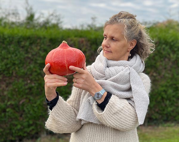 Béa, fondatrice de Femmes en Harmonie, contemplant un potimarron dans son jardin. 