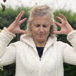 Béa, fondatrice de Femmes en Harmonie, dans son jardin illustrant les premiers signes de la ménopause avec une expression de stress et de tension, et représentant les défis émotionnels et physiques liés à cette étape.