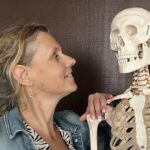 Béa, fondatrice de Femmes en Harmonie, souriante et complice avec un squelette en référence au temps qui passe, illustrant l'importance d'un état d’esprit positif en prenant de l'âge.