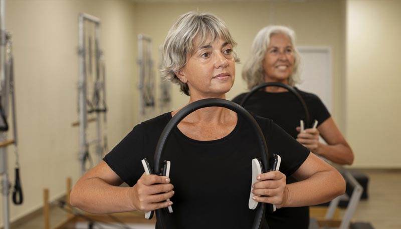 Deux femmes d'environ 50 et 60 ans pratiquant des exercices en utilisant un anneau de fitness. 