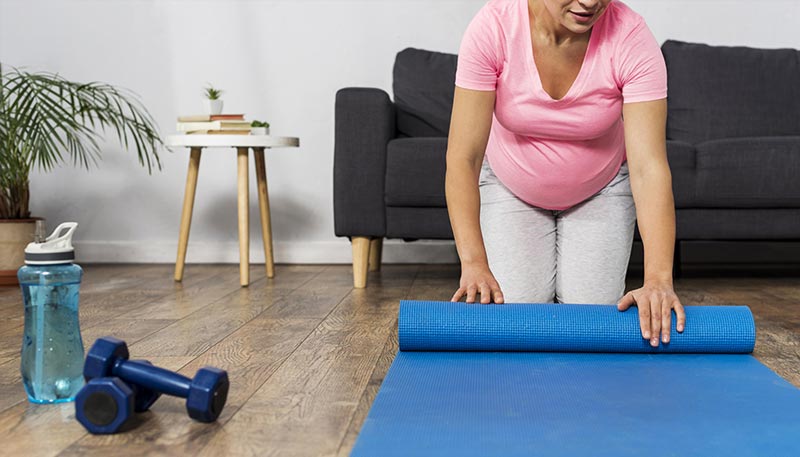 Une femme de 50 ou 60 ans déroulant un tapis de yoga chez elle, prête pour des exercices de musculation pour les femmes, afin d’améliorer son équilibre, sa coordination et sa stabilité au quotidien.