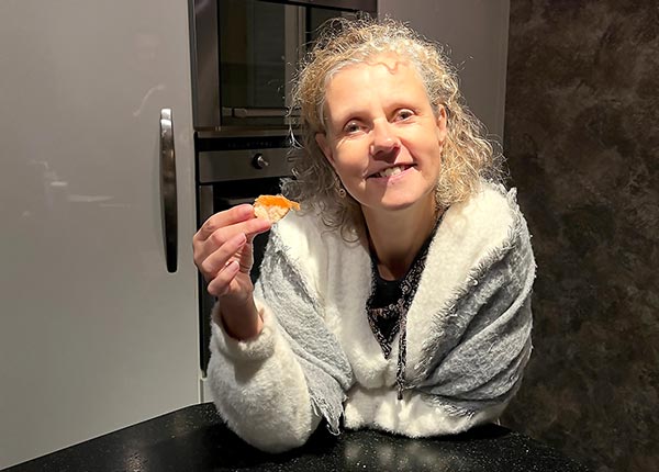 Béa, fondatrice de Femmes en Harmonie, avec un grand sourire dans sa cuisine, tenant dans sa main un toast avec du saumon. Elle partage des conseils sur les meilleures sources de calcium pour une santé osseuse optimale après 45 ans. 