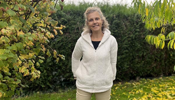 Béa debout dans son jardin, sereine et souriante, dans l'acceptation de cette période délicate pour les femmes.