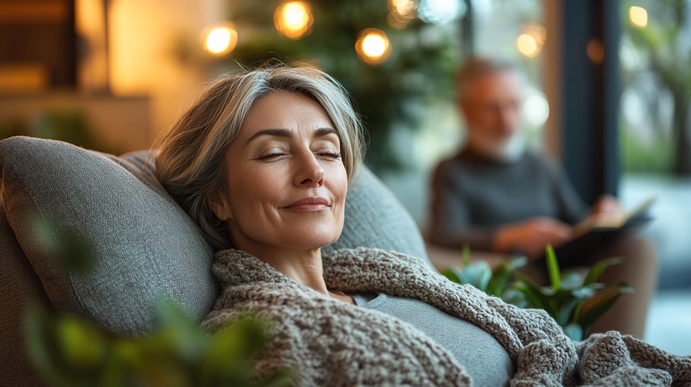 Femme d'environ 50 ans, assise paisiblement les yeux fermés dans un fauteuil, profitant d’un moment de détente et de reconnexion grâce aux bienfaits de l’hypnose. L’ambiance douce et naturelle symbolise l’apaisement, la gestion des émotions, et la réduction du stress.

