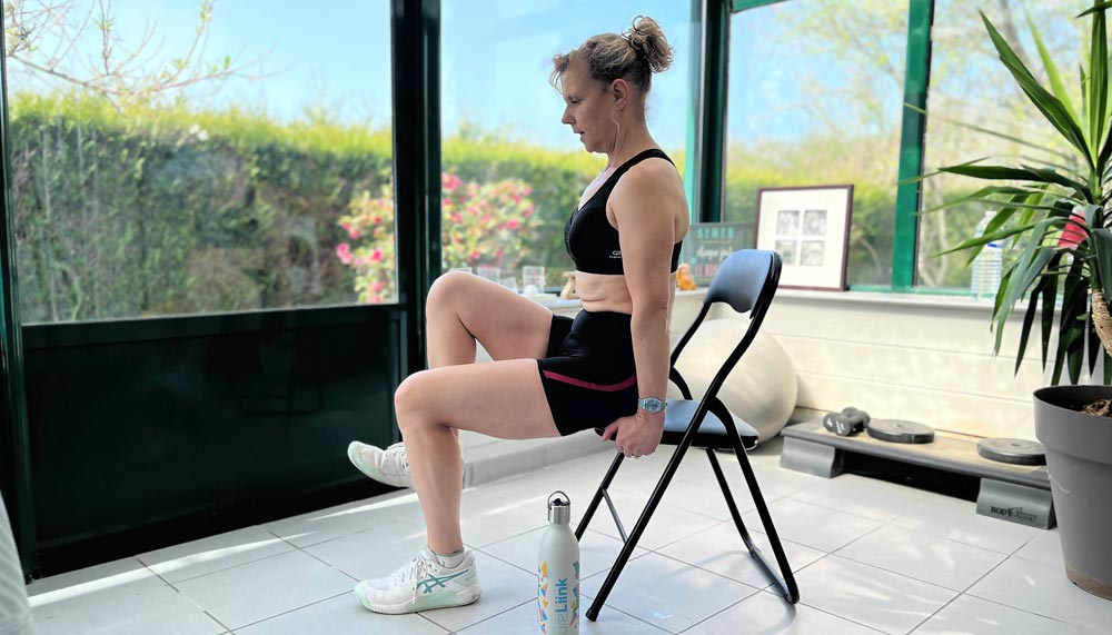 Béa, créatrice de Femmes en Harmonie, réalise un exercice de levée alternée des genoux sur chaise, idéal après 50 ans pour renforcer les abdominaux en douceur.