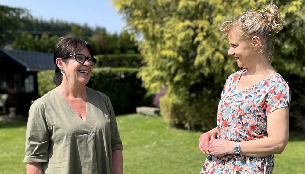 Béa, fondatrice de Femmes en Harmonie, en pleine discussion avec Françoise, 71 ans, dans un jardin verdoyant. À travers l’activité physique, une alimentation plus saine et un nouveau regard sur elle-même, Françoise a retrouvé souplesse, confiance, légèreté, et une profonde sensation de bien-être après 60 ans.