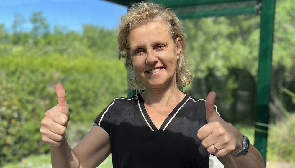 Béa, la créatrice de Femmes en Harmonie, souriante et levant les pouces avec assurance et bienveillance, dans une véranda lumineuse. Sa posture évoque la réussite progressive pour retrouver une relation saine et sereine avec la nourriture et avancer vers plus de liberté.